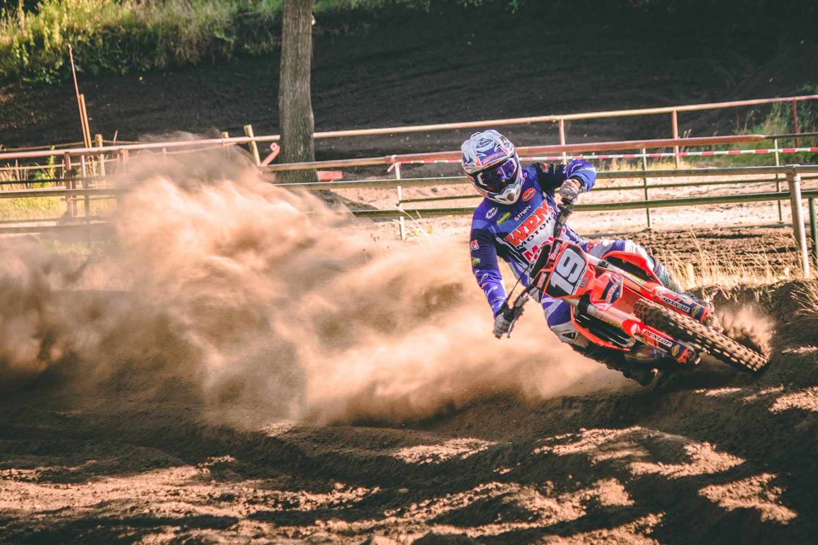 A motocross rider cornering hard, rear wheel throwing a wall of dirt